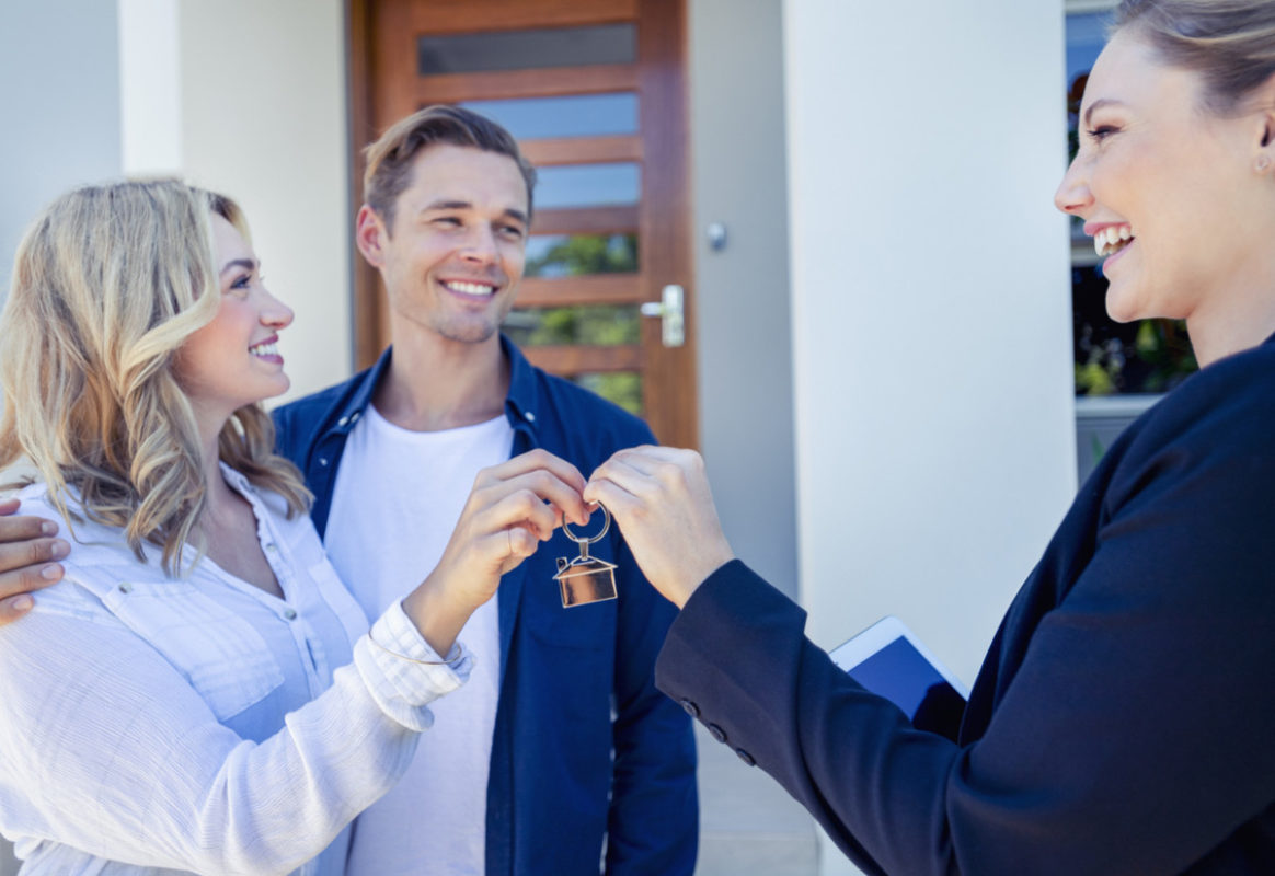 Real estate agent giving a young couple the key to their new house.